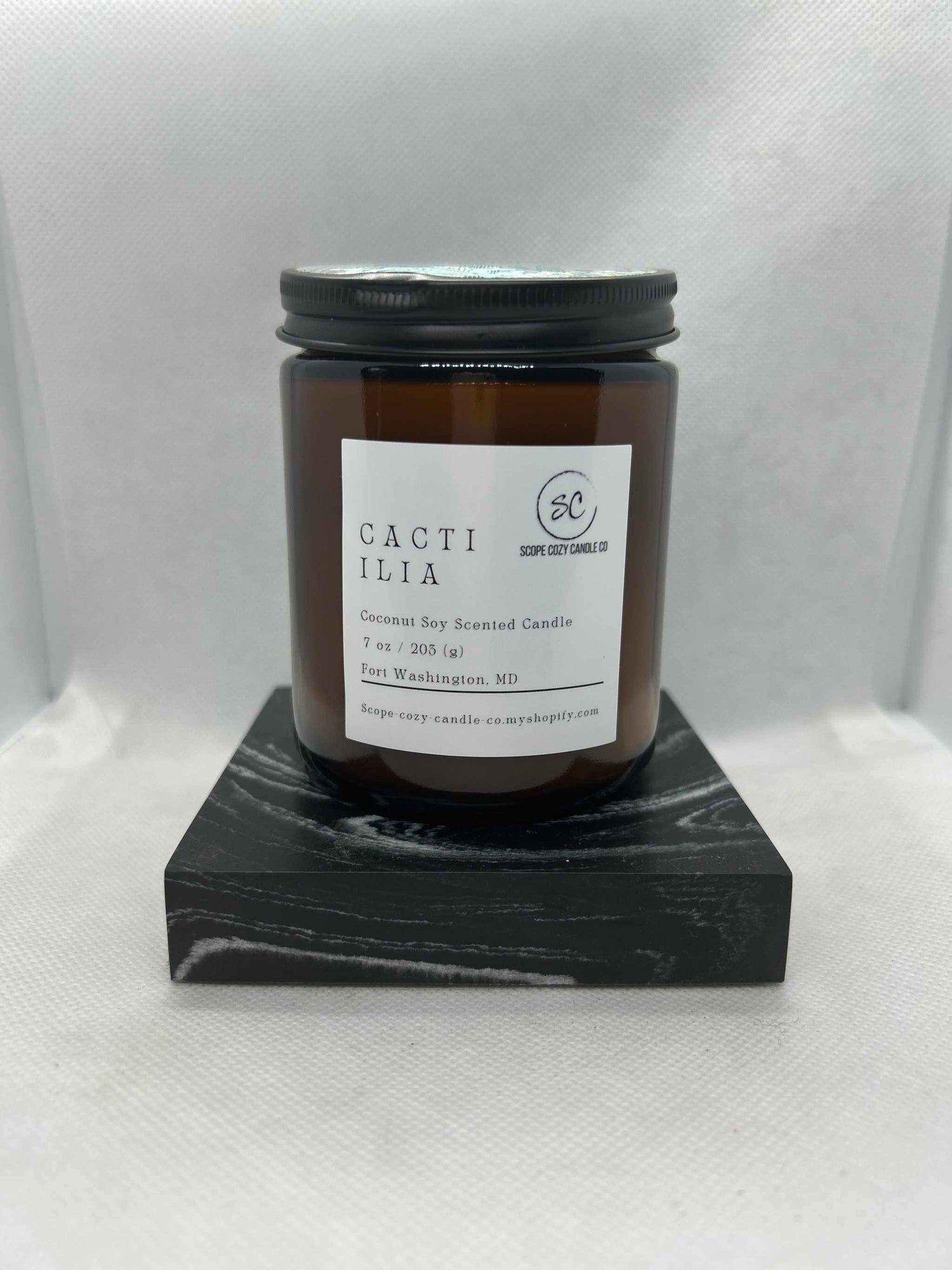 Cacti Ilia Coconut soy scented candle in amber glass jar with black lid on black wooden stand