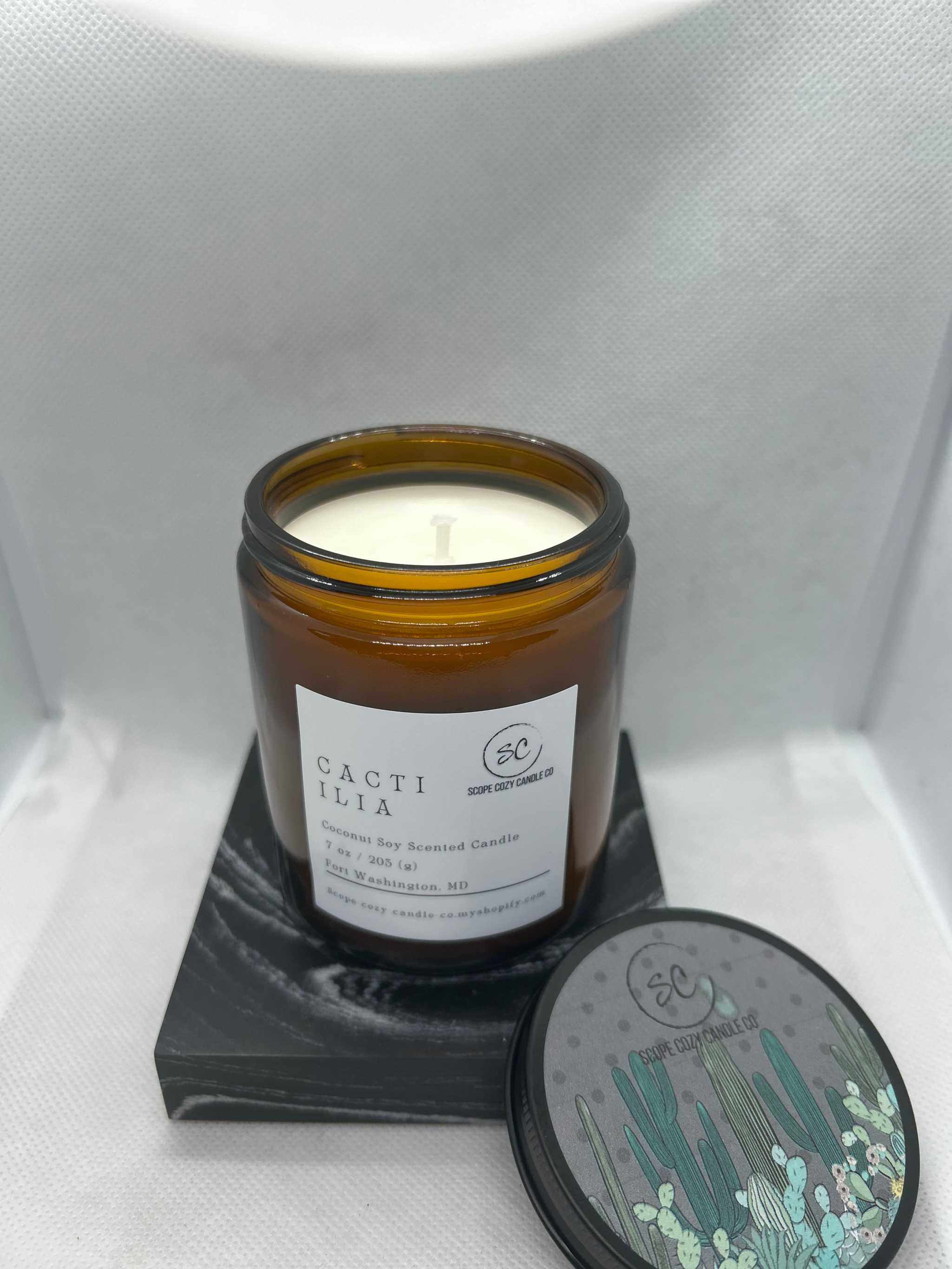 Cacti Ilia Coconut soy scented candle in amber jar with cactus-themed lid on black coaster